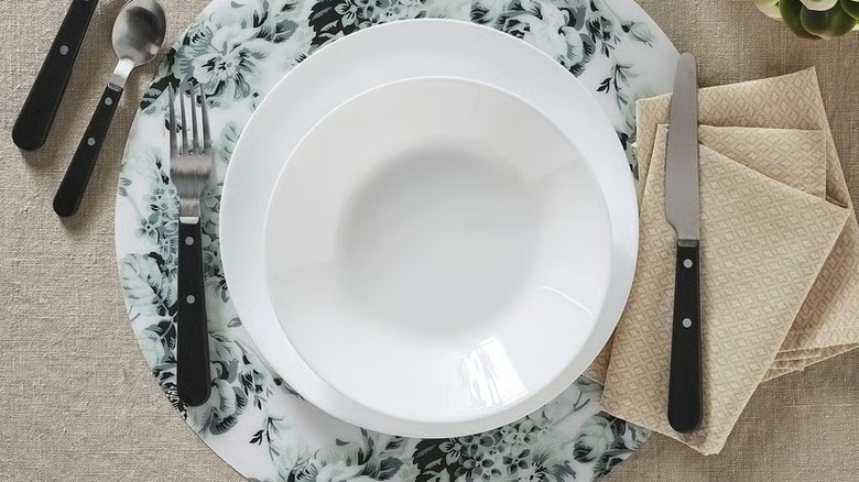 Two white plates nested over a floral placemat holding utensils