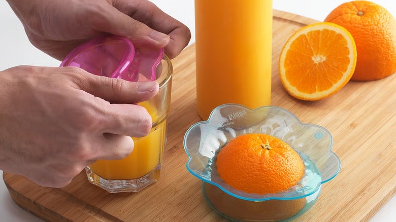 Hand putting a pink silicone food cover over a glass juice