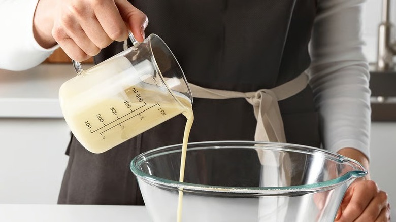 Hand pouring batter into a glass bowl using a measuring cup