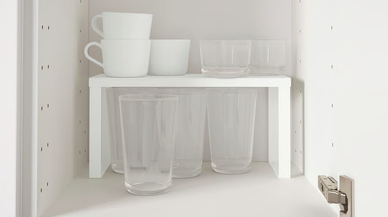 A white shelf insert inside a cabinet with cups on top and glass beneath it