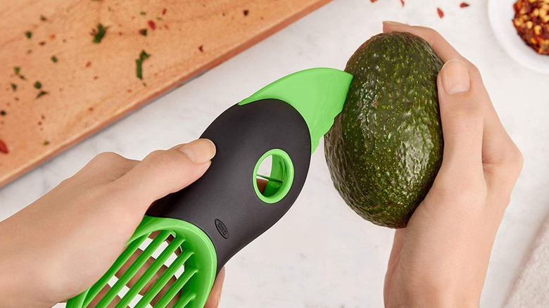 Hands holding a green avocado slicer inserted into an avocado