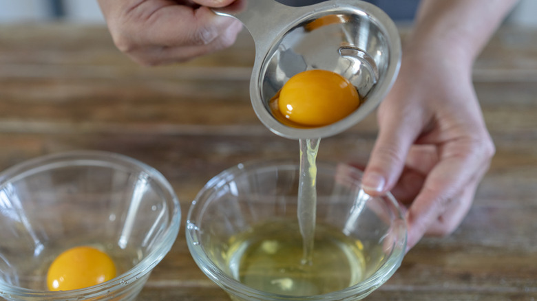 person seperating an egg white and egg yolk into bowl