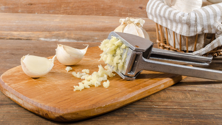 garlic press resting on a wooden chopping board