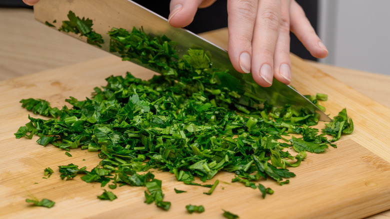 person chopping herbs with a knife on chopping board