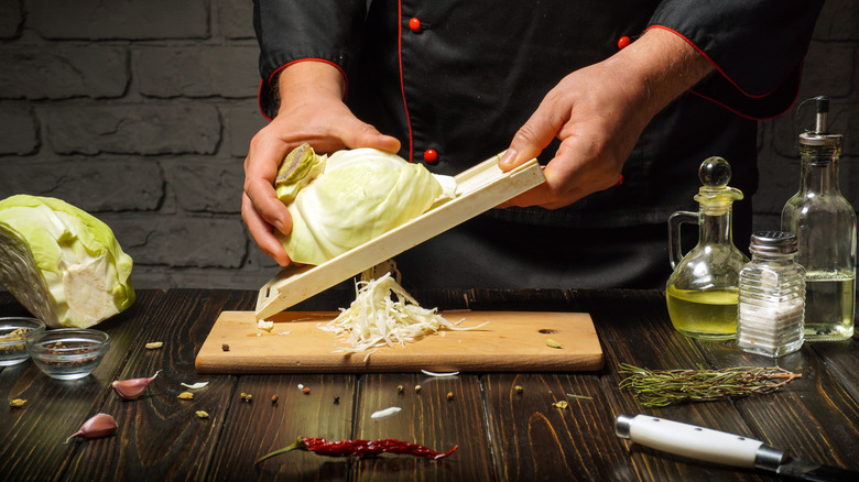 person holding a mandoline and slicing a white cabbage