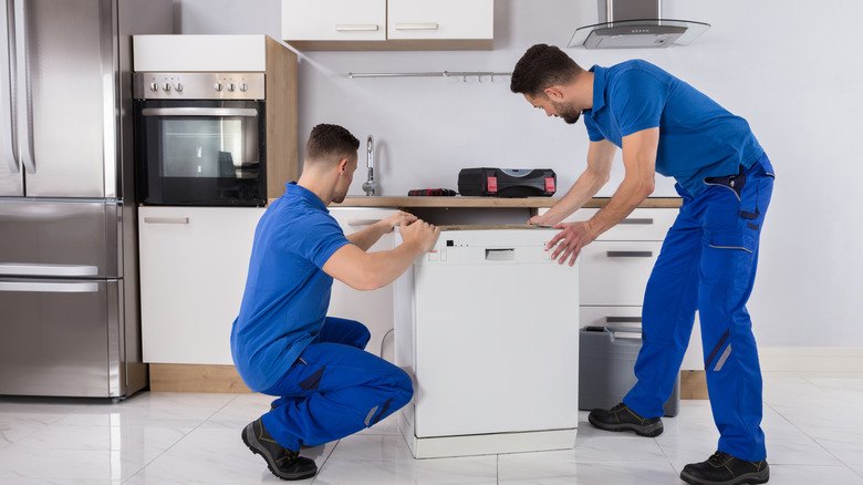 Two men in blue installing a new dishwasher.