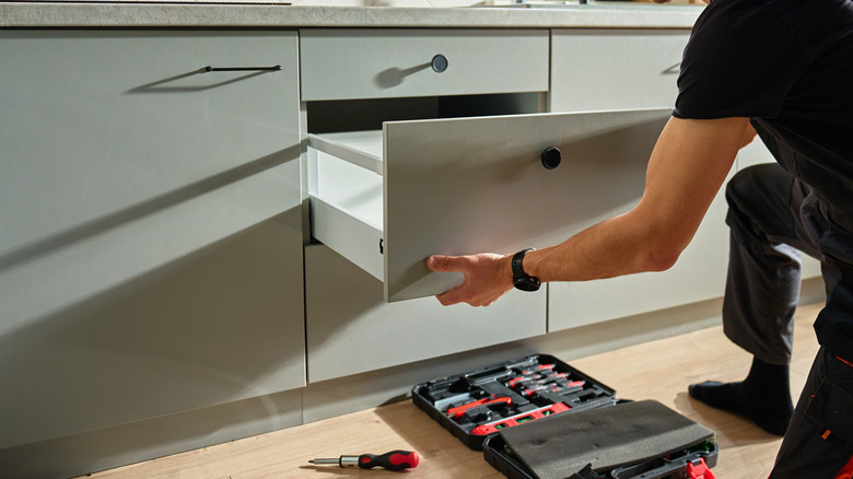Hands installing builder grade kitchen cabinets.