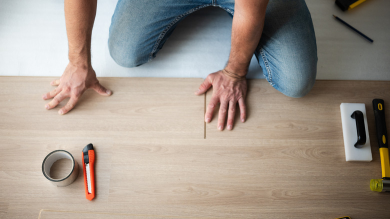Hands installing hardwood floor planks.
