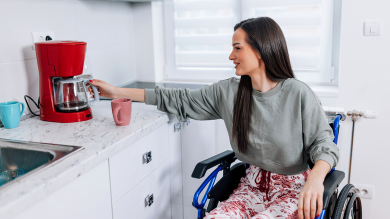 A young Caucasian woman in a wheelchair is preparing coffee in the kitchen