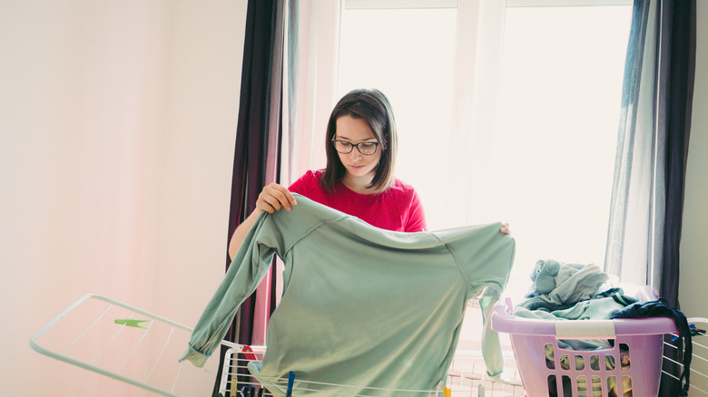 A woman handing a pale green sweater on a drying rack
