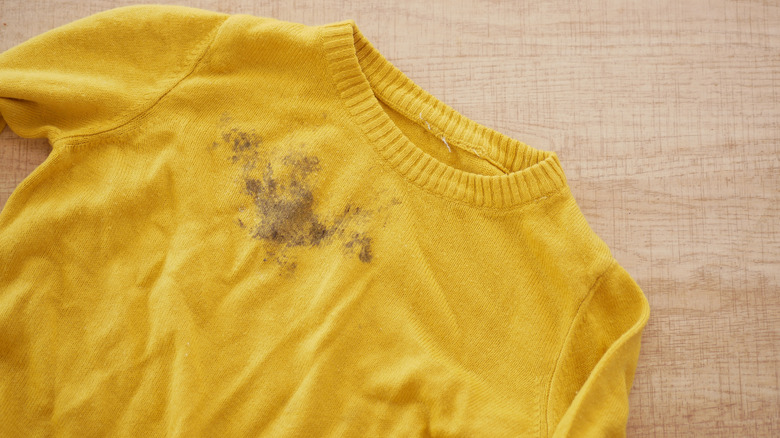 A yellow sweater laying on a beige surface with a brown stain