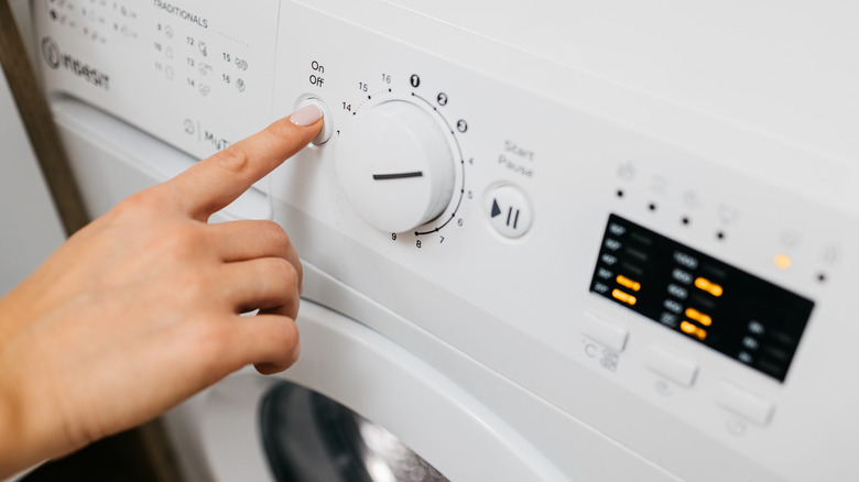 A person pressing the on off button on a white front loader washing machine