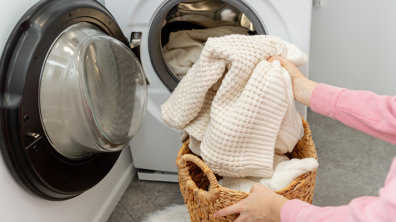 A person loading a white wool sweater into a front loader washing machine