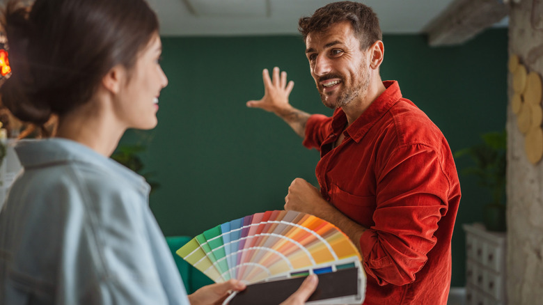A woman holding paint swatches and a man gesturing to a wall.