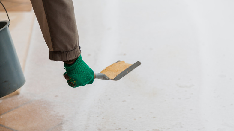 Hand applying sand on snow using a bucket and small shovel