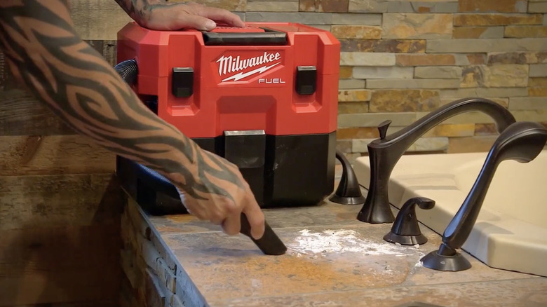 A person cleaning a work surface with Milwaukee's M12 Lithium-Ion Cordless 1.6-Gallon Wet/Dry Vacuum