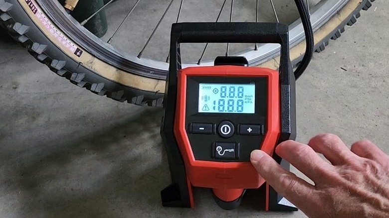 Close-up of a person using Milwaukee's M12 Lithium-Ion Cordless Electric Portable Inflator on a bike tire
