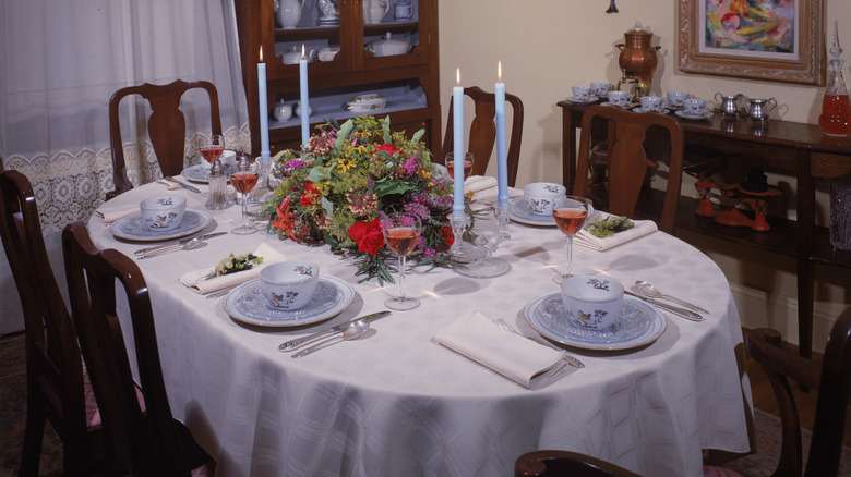 A dining table set with fine china, candles, and a large floral arrangement