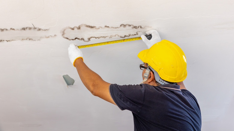 A person measuring water stains on a wall.