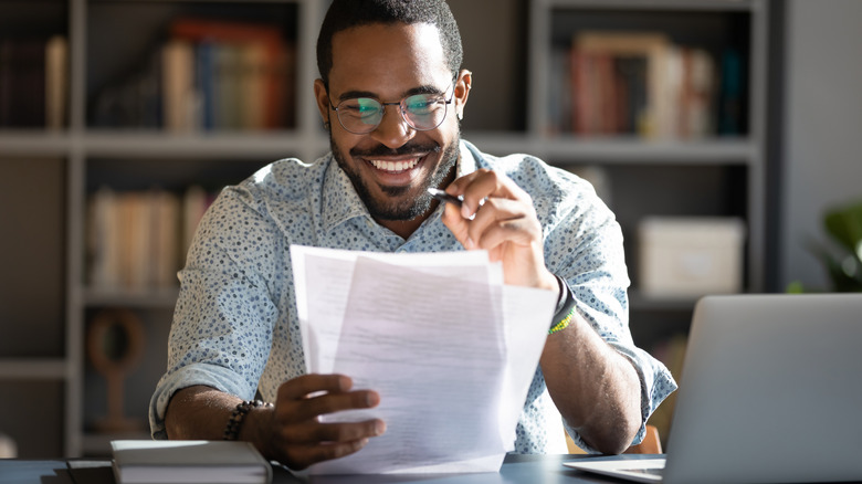 A person sitting at a desk looking at a document and smiling.