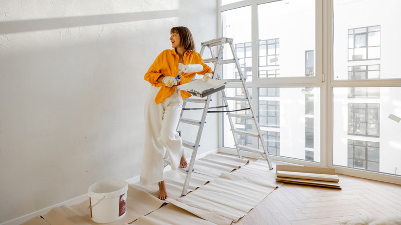 Woman standing on a ladder holding a paint roller and tray