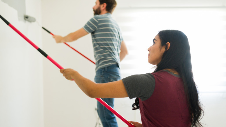 Young couple using paint rollers with extension poles to paint a wall