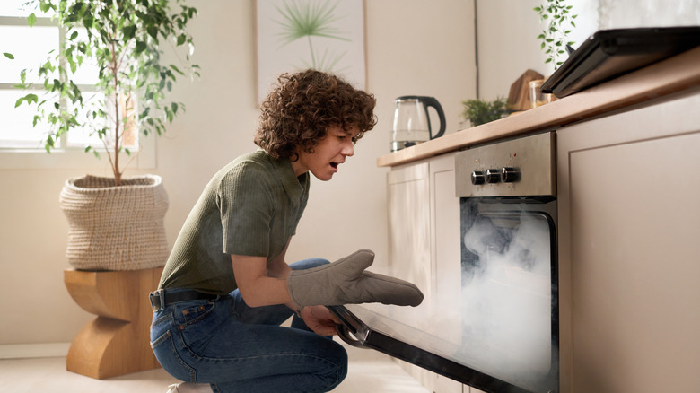 A woman is staring in dismay at a smoke-filled oven