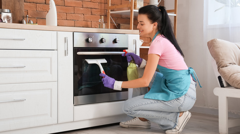 A woman is cleaning her glass oven door with sprayed water and a squeegee tool