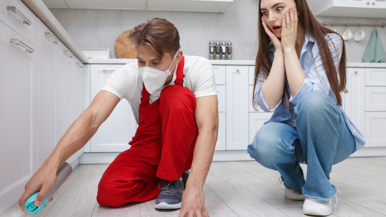 A woman watches worriedly as a pest control professional sprays for termites in her kitchen