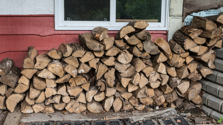 A woodpile is stacked directly against a house with red wooden siding and white plaster
