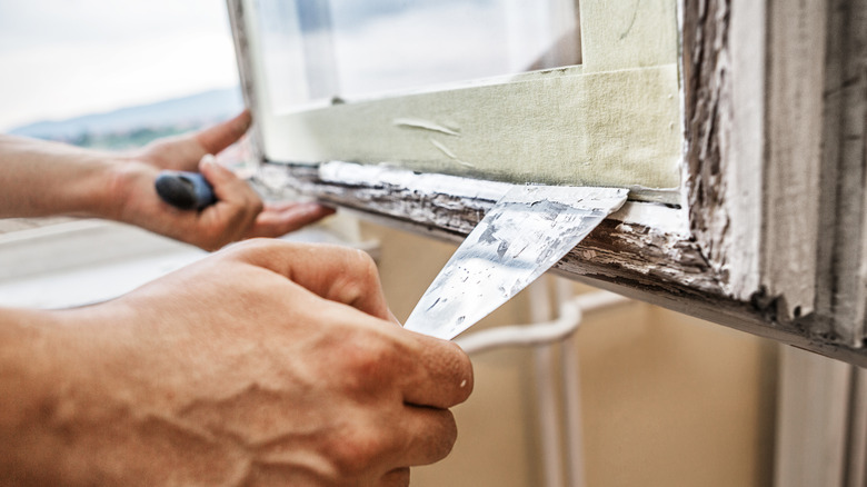 A person is scraping old paint from a window in preparation for repairing it