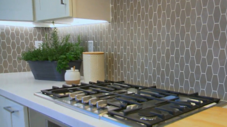 Grey honeycomb tile backsplash with a range and white cabinets and decor items on the counter