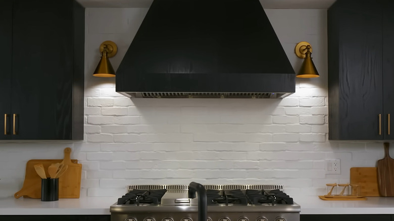 A white brick backsplash with a dark wood hood and cabinets over a range