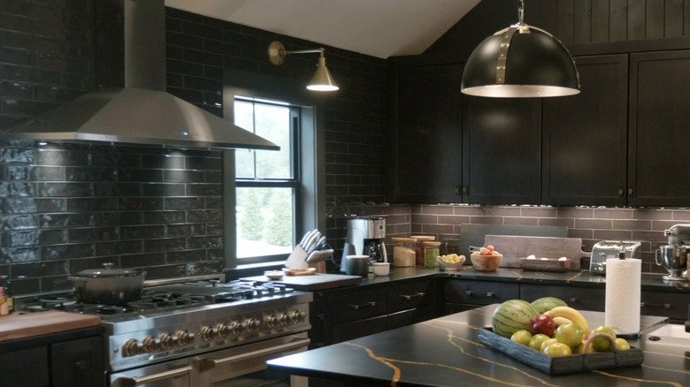 Black subway tile in a kitchen with stainless steel range and hood and kitchen island in the foreground