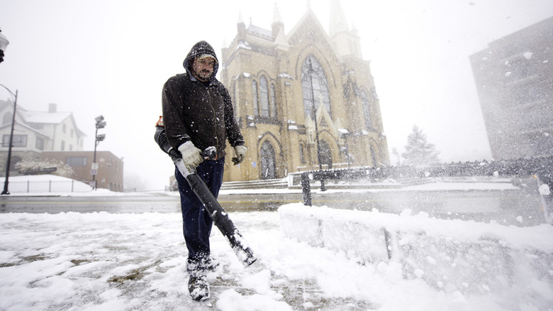 Man cleans pavement from snow with blower