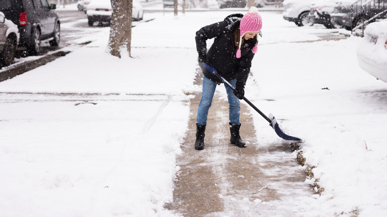 Woman in pink hat shoveling snowy sidewalk