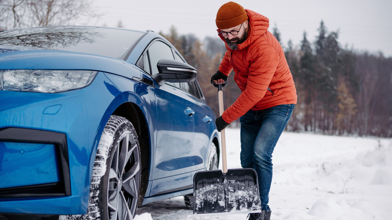 Man shoveling snow next to blue car