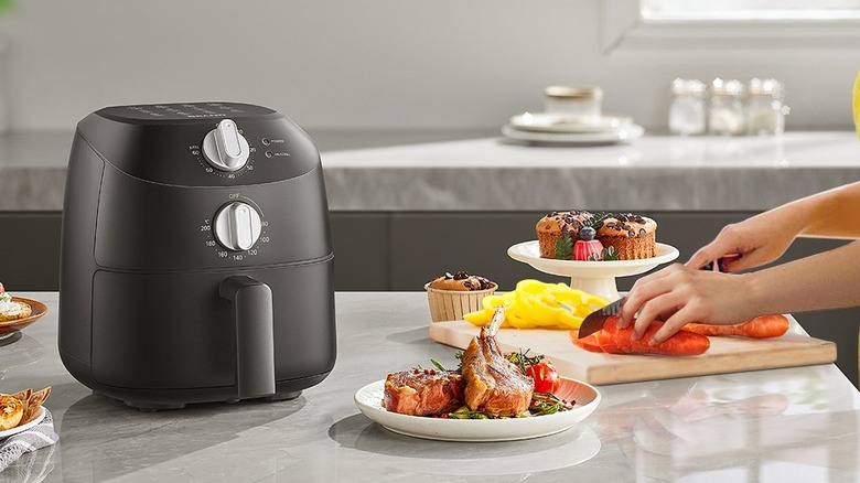 A black air fryer on a kitchen counter laden with food plates