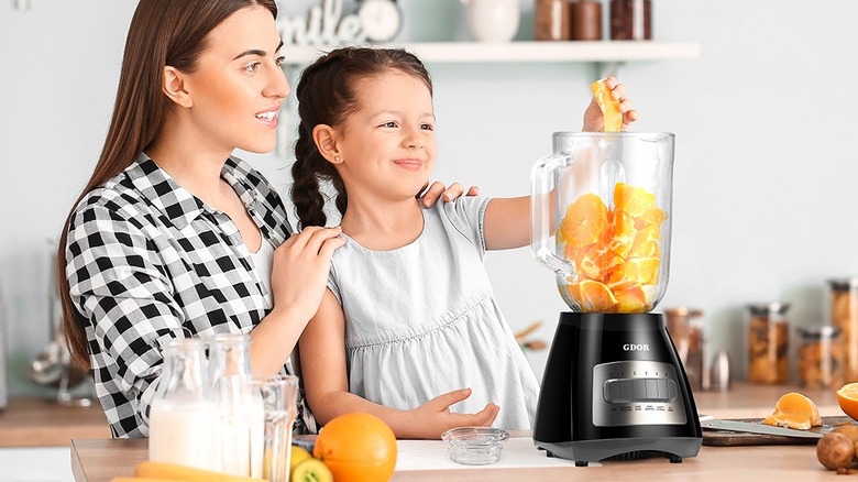 Mother and daughter adding orange slices in a blender