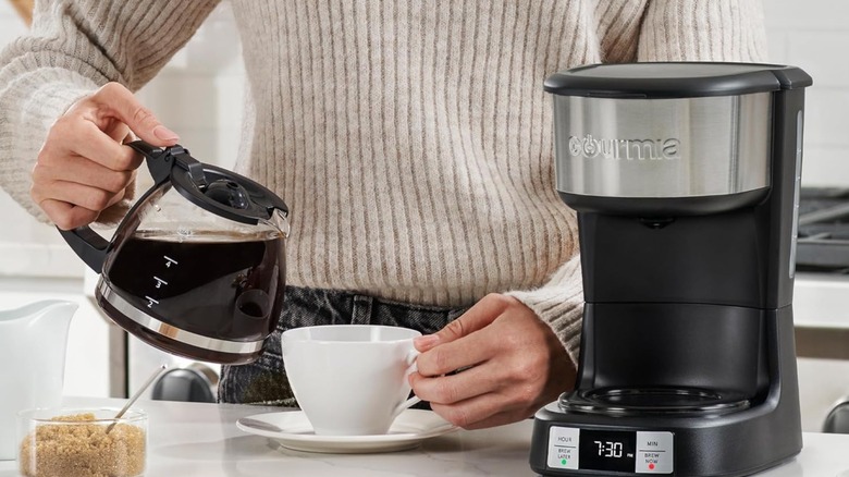 Hand pouring a cup of coffee near a drip coffee maker