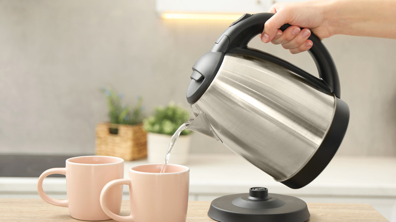 Hand pouring water into two cups from an electric kettle