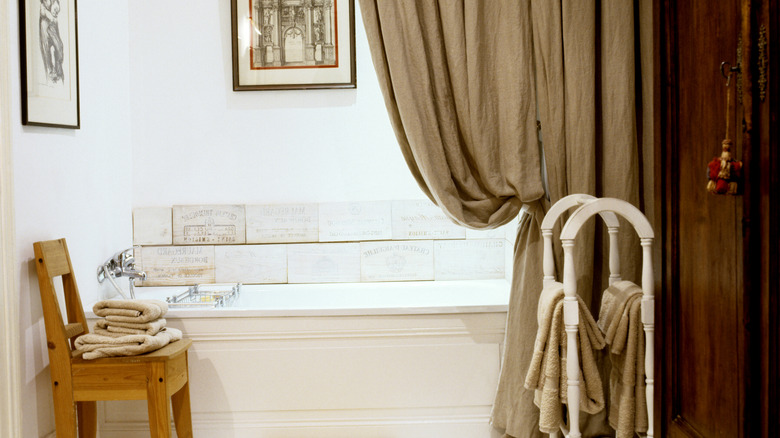 A long, greige curtain pulled back from a rustic tub