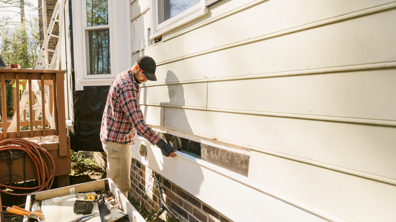 Person repairing the siding on a house.