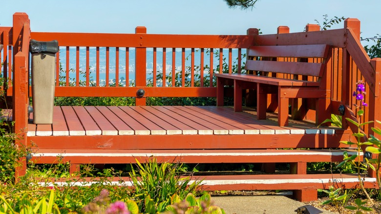 Red wooden deck with bench and wooden hand rails that lead down steps.