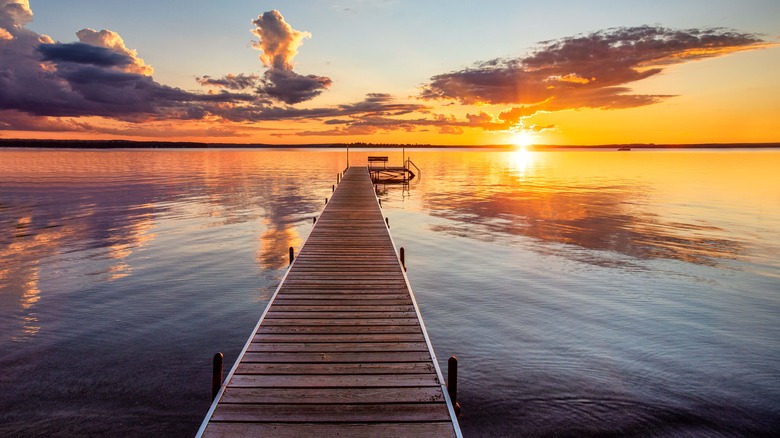 A dock extending out on a lake at sunset with clouds in sky