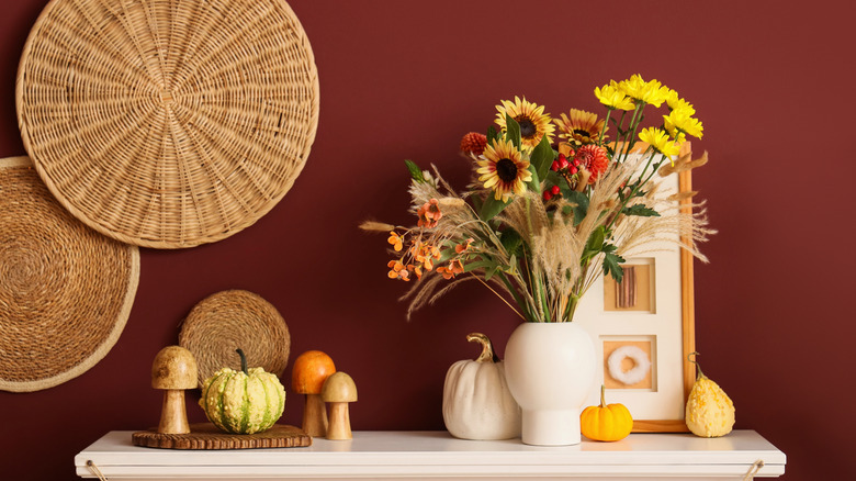 Burgundy painted wall with vase and dried flowers with raffia circles on the wall.