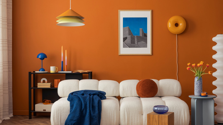 Burnt orange wall with retro 79s sofa, lamps and wall hangings.