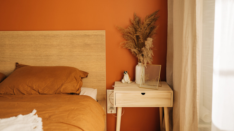 A pine bed with burnt sienna walls and a retro wood bedside table