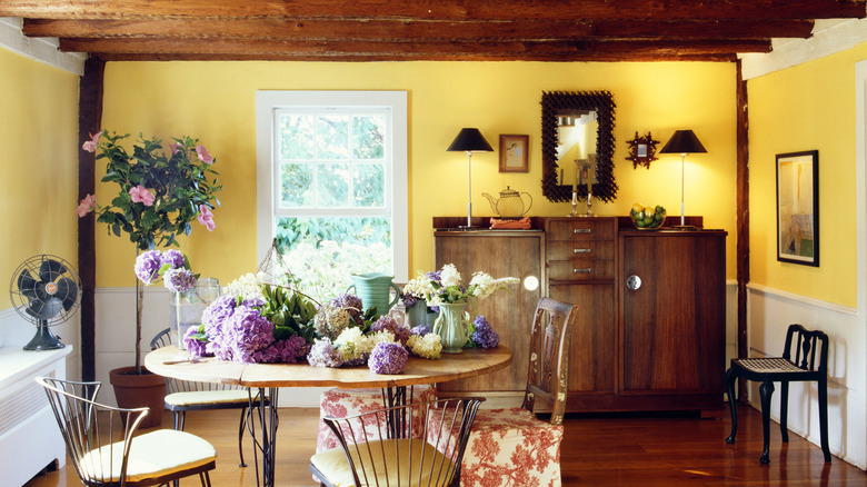 A sunny yellow room with mid-century sideboard, table and chairs with flowers on top of the table.