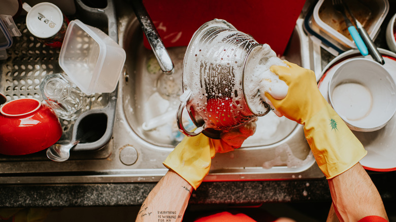 someone with yellow gloves handwashing a steel strainer